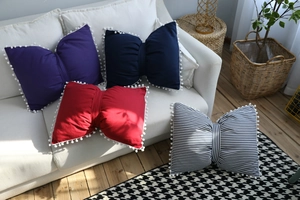 Close-up of bow-shaped decorative pillows with white pom-pom trim in four different colors