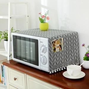 Detail of microwave dust cover with grey herringbone pattern, side pocket and pom-poms