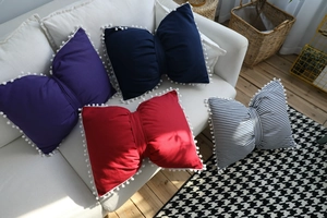 Close-up of bow-shaped pillows with pom-pom edges in various colors on a sofa