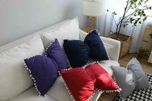 Detail of bow-shaped decorative pillows with pom-pom trim on a white sofa