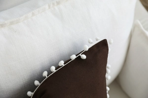 Macro detail of dark coffee striped cushion fabric featuring white pom-pom trim edges