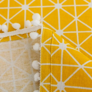 Macro detail of yellow geometric tablecloth featuring white pom-pom trim and fabric texture