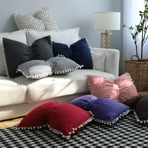 Bow-shaped striped decorative throw pillows with pom-pom trim in cozy home setting