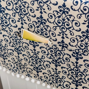 Détail du motif floral damassé bleu sur tissu beige avec bordure à pompons blancs