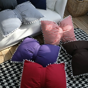 Bow-shaped striped pillows with pom-pom trim in various colors on a modern sofa