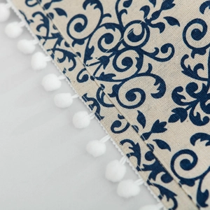 Détail macro du motif floral bleu sur tissu en lin beige avec bordure à pompons blancs