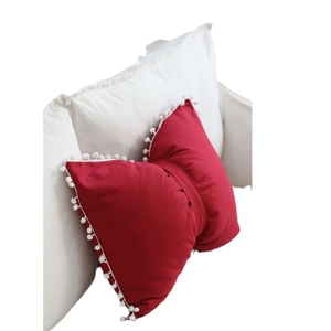 Red bow-shaped pillow with white pom-poms on a white sofa in a minimalist Nordic style