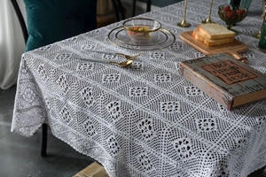 Close-up detail of white crochet lace tablecloth with hollow floral pattern and scalloped edges