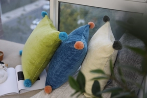 Detail of soft velvet cushion covers with fluffy colorful pom-poms on the corners