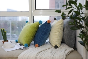 Detailed texture of velvet pillows with colorful pom-poms in a cozy home setting