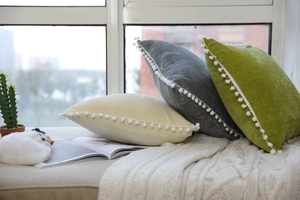 Close-up of soft velvet throw pillows with white pom-pom trim in diverse colors