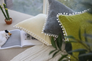 Detailed view of Nordic velvet pillows in yellow, grey, and green with white pom-pom edges