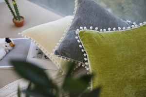 Detail showing soft velvet pillows with pom-pom trim in green, grey, and beige