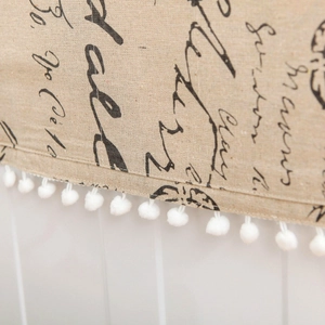 Close-up of beige linen fridge cover featuring pom-pom fringe and vintage black script