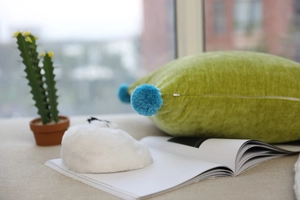 Detail of soft green velvet cushion with blue pom-poms on a sunny windowsill