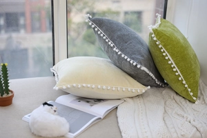 Close-up of velvet decorative cushions with soft pom-pom trim in beige and green