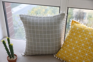 Detail of cotton linen pillowcase with white pom-pom fringe and geometric pattern