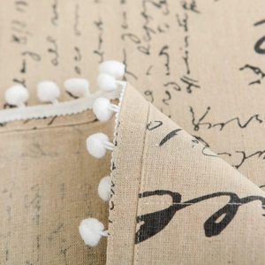Close-up of linen fabric dust cover with printed text and white pom-pom lace trim