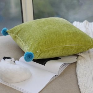 Detail of avocado green velvet pillow with blue pom poms and hidden zipper closure