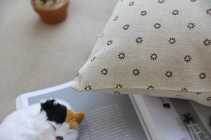Detail der floralen beigen Kissenhülle aus Leinen mit warmer Deko und Katzenplüschhintergrund