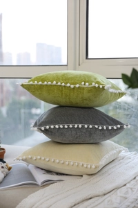 Detailed view of velvet cushions in green, grey, and cream with decorative white pom-poms