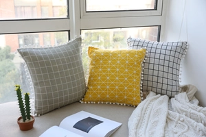 Detail of Nordic cotton linen pillow covers with pom-pom edges on a bright windowsill