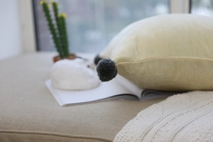 Detail showing soft light yellow velvet pillow texture and grey pom-pom corner decoration