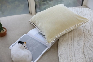 Detail of cream velvet pillow cover with white pom-pom edges in a cozy home setting