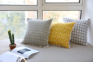 Close-up of geometric cotton linen pillows featuring white pom-pom fringe details