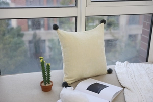 Detail of soft velvet cushion with grey pom-pom corners on a bright window sill
