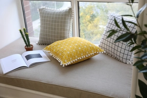 Detail of geometric cotton linen cushions with white pom-pom fringe in a home setting