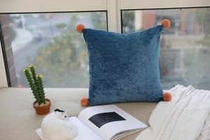 Detailed view of blue velvet pillow with soft texture and pink corner pom-poms decor