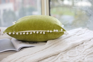 Detailed close-up of velvet olive green pillow with white pompom fringe and hidden zipper
