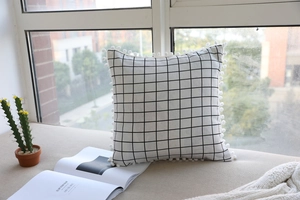 Detail of checkered linen lumbar pillow with white decorative pom-poms in a cozy setting
