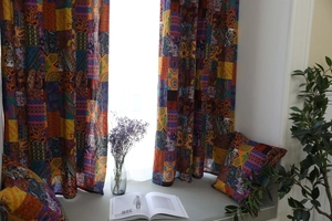 Dettaglio di tende patchwork boho con motivi paisley e cuscino coordinato nella luce solare