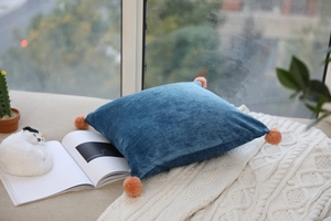 Detail of soft blue velvet pillow with orange pom-poms on a cozy white knit blanket
