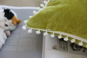 Detail of green velvet pillow cover showing invisible zipper and white pom pom fringe