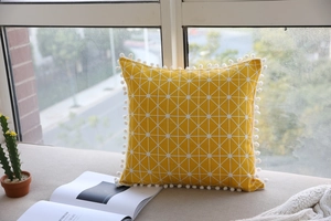 Detail of yellow geometric linen pillow with white decorative pompoms on a sunlit window