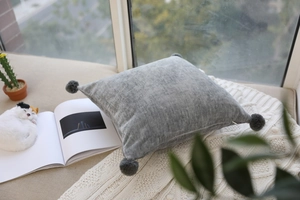 Close-up of gray velvet pillow with decorative pom-poms on a cozy window sill setting