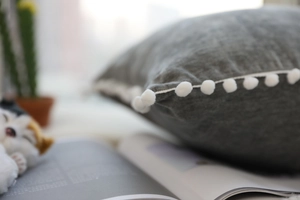 Macro view of grey velvet cushion with white pom-pom trim and detailed fabric texture
