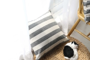 Detail of grey and white striped cushion cover resting on straw mat by window
