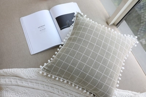 Close-up of geometric linen pillow with white pom-pom trim and plaid pattern texture