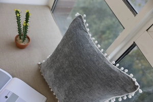 Detail of grey velvet cushion cover with white pom-pom trim on a cozy windowsill