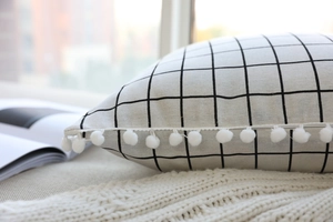 Detail of grid linen pillowcase with decorative white pom-pom trim for home decor