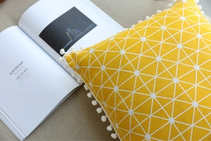 Detailed texture of yellow cotton linen pillow with white geometric pattern and pom-poms