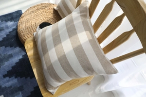 Detail view of beige striped cotton linen cushion cover on a wooden chair with soft sunlight