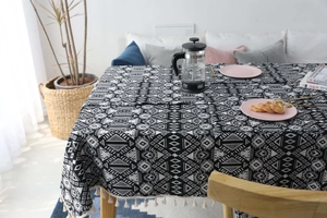 Dettaglio tovaglia nordica geometrica in bianco e nero con nappe bianche su tavolo in legno