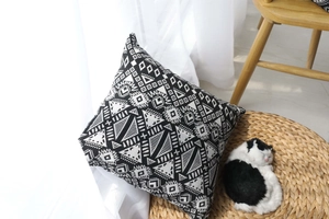 Detail of black and white geometric ethnic cushion on woven mat with cat ornament