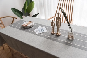 Detail of grey European tablecloth featuring embroidered stripes and elegant white tassels