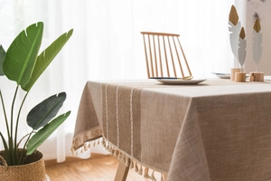 Detail shot of modern linen tablecloth with elegant white embroidery and tassel fringe